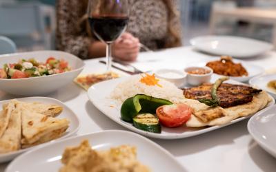 A couple sitting at a restaurant enjoying a Mediterranean dish served on a plate with a glass of red wine.