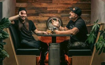 Two men sitting at a table across from each other drinking craft beer.