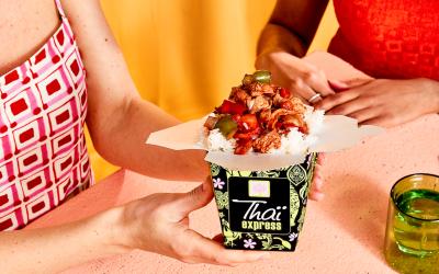 Two people sitting at a table enjoying Thai food from a takeout container.